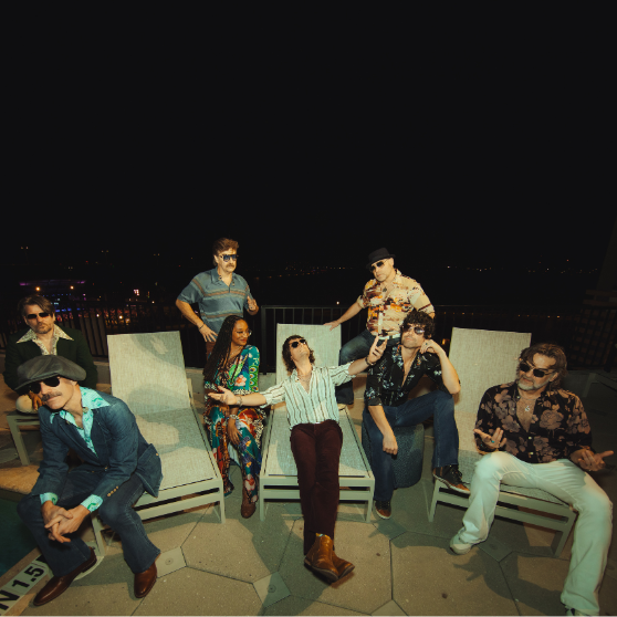 Nine adults lounge on poolside chaise chairs at night, wearing retro-patterned outfits and sunglasses. Several hold drinks, with city lights and dark sky in the background.