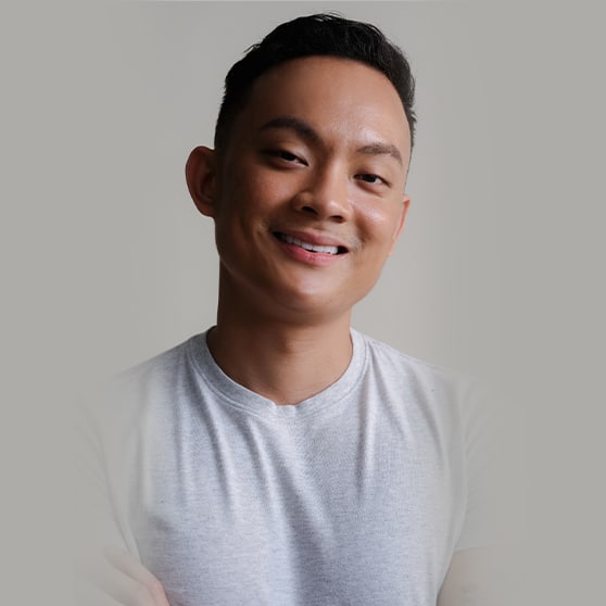 A person wearing a light gray t-shirt standing against a plain gray background with their arms crossed.
